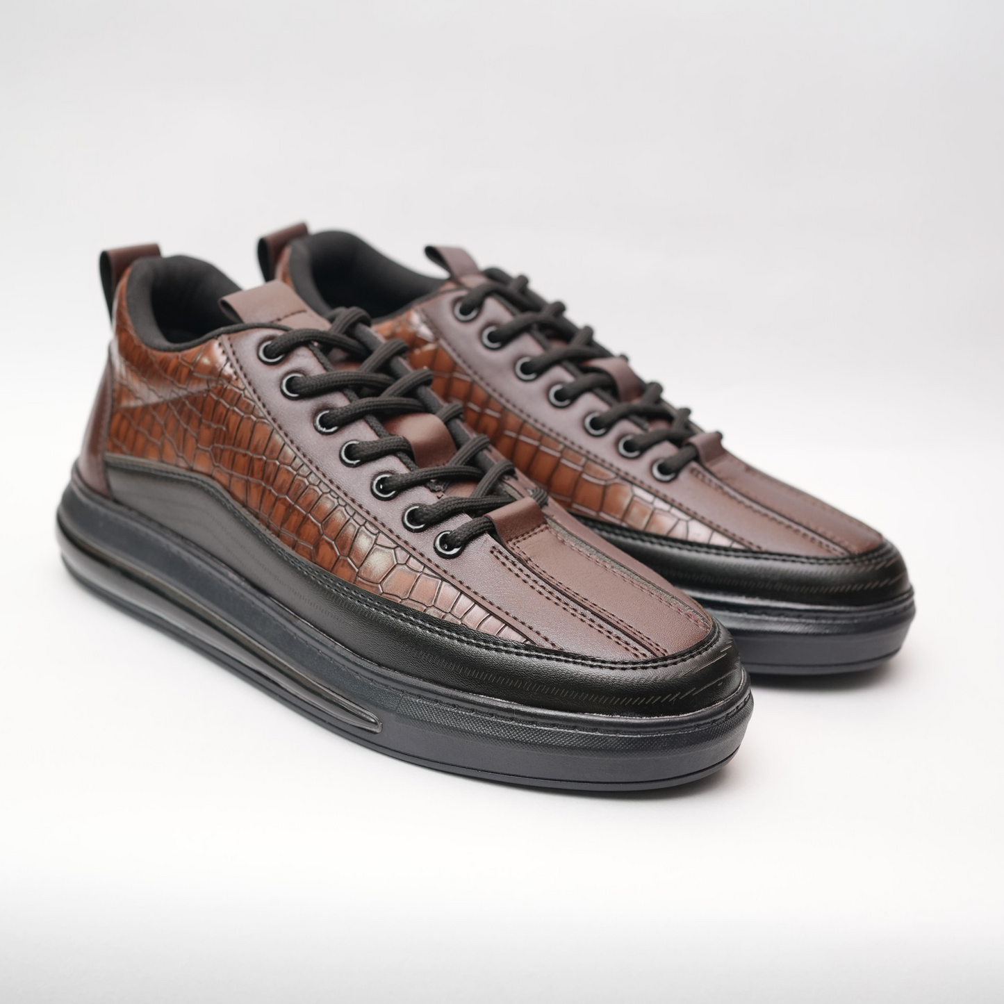 Pair of brown leather sneakers with black soles on a light gray background